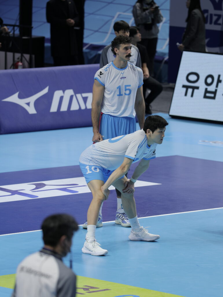 Volleyball players preparing for serve in a competitive match setting.